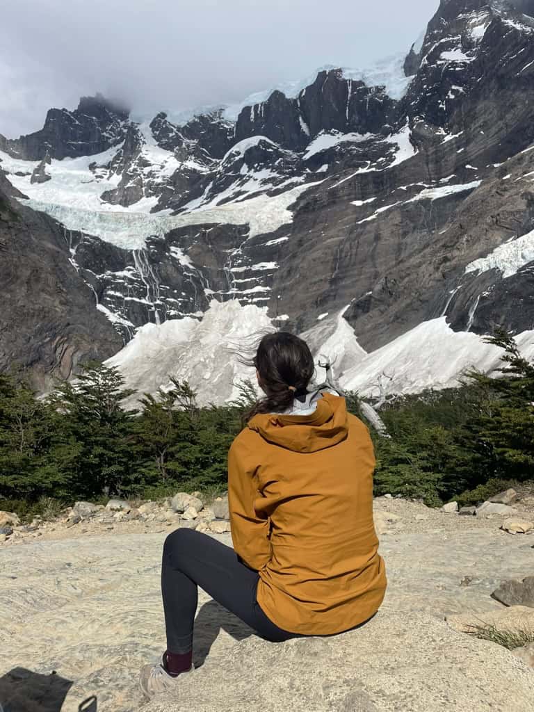 girl in orange jacket looking at a glacier on snow capped rocky mountain called Mirador Frances Lookout in Patagonia on a 2 week trip