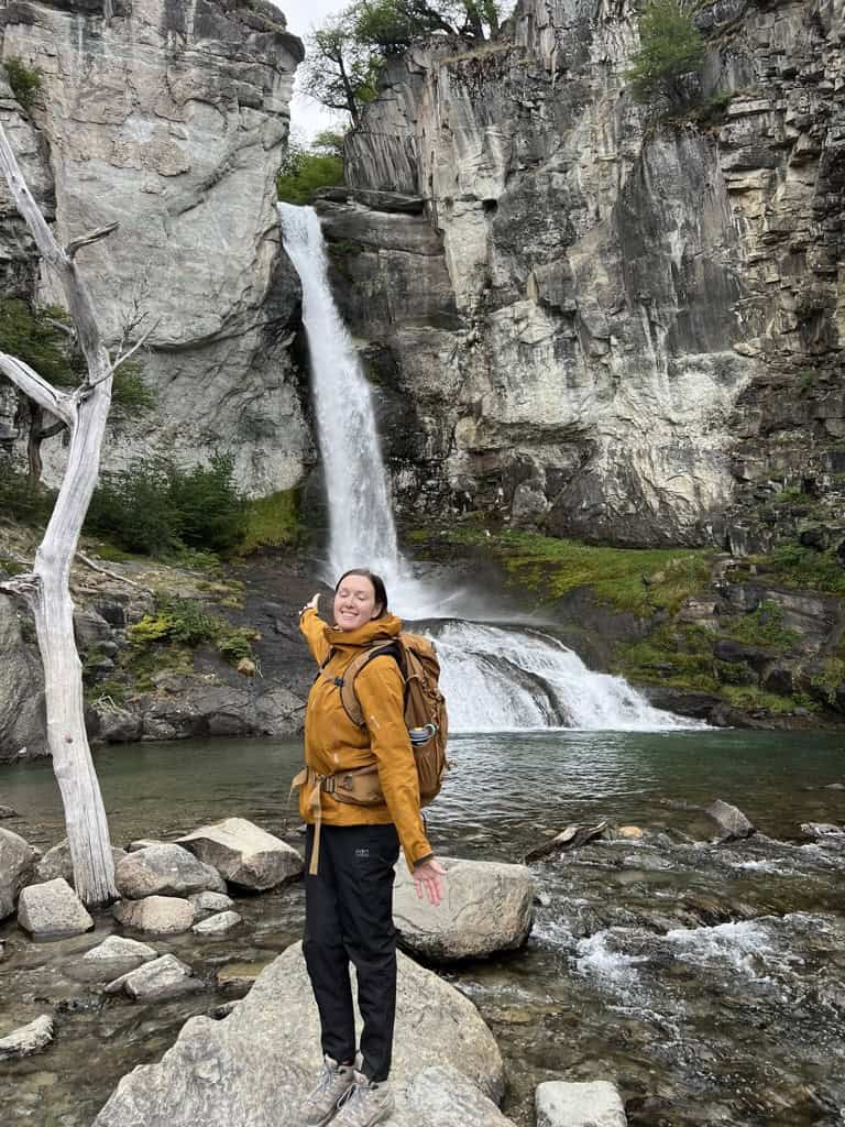 female in orange jacket infront of waterfall in Patagonia