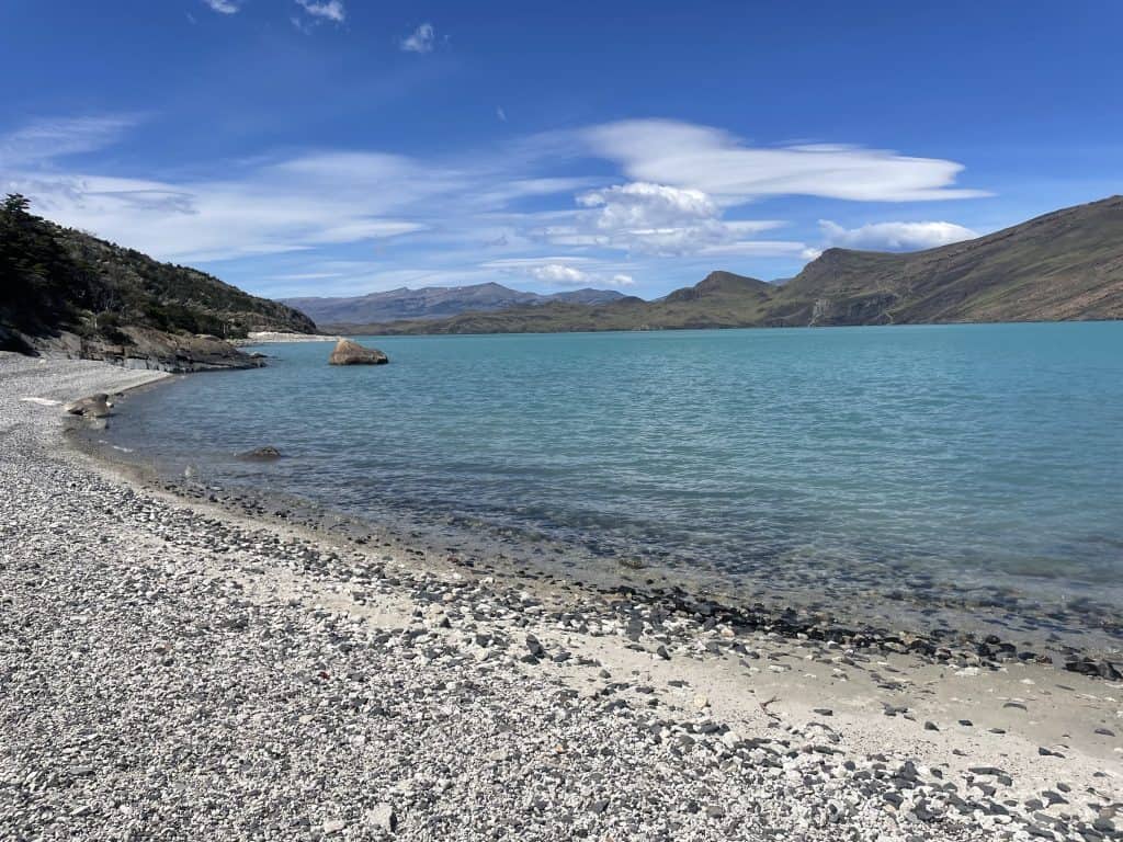 Beach shot of Lake Nordenskjöld with stone pebbles along the waterline met with three different shades of blue water in Patagonia