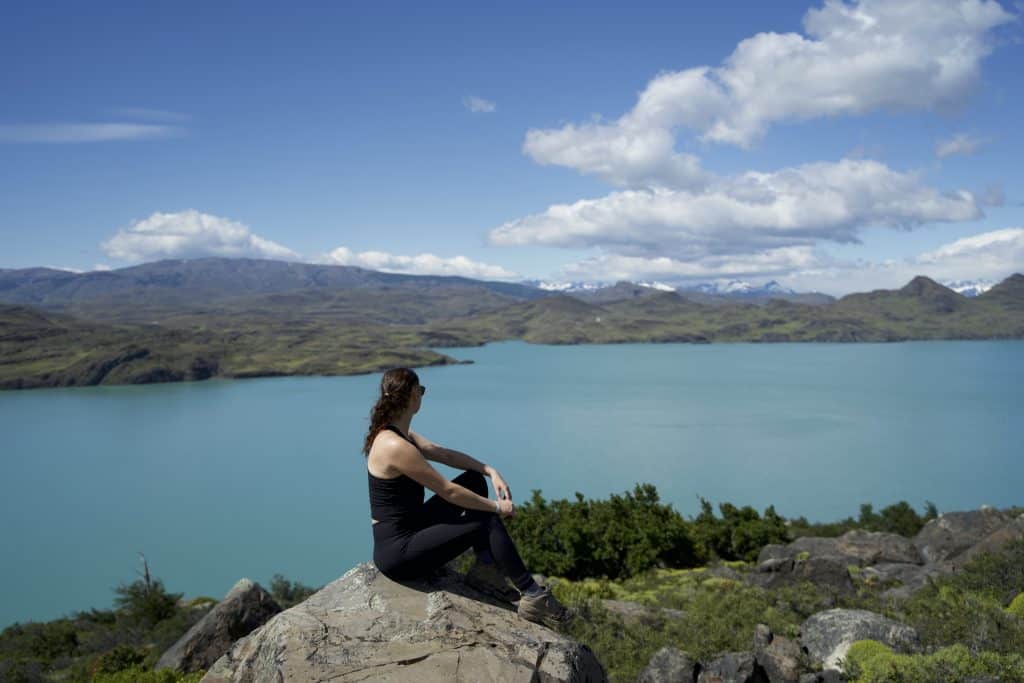 hiker sitting on rock looking out to blue turquoise lake on the W Trek in Patagonia for 2 weeks