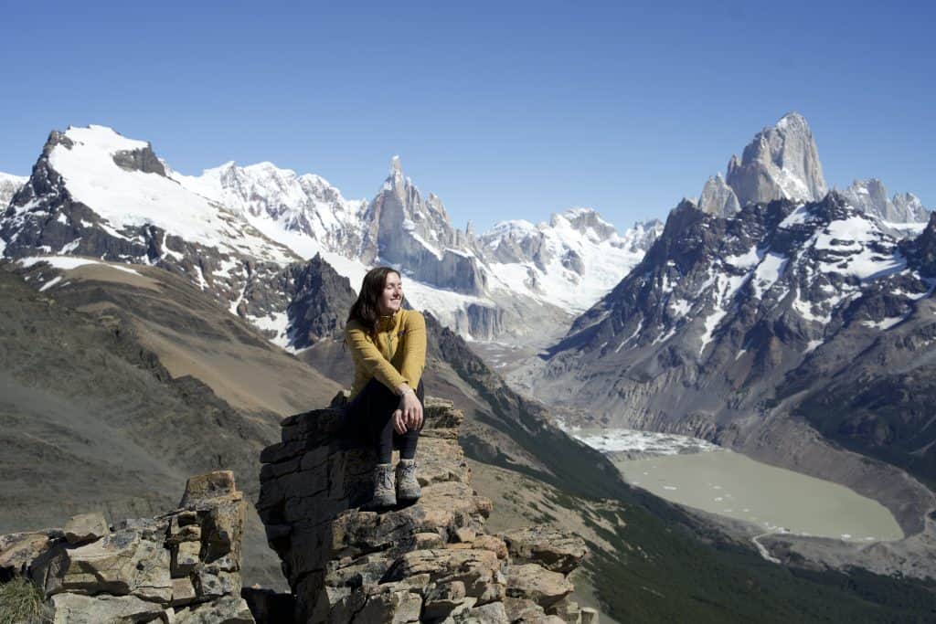 female in yellow sweater at the top of a mountain summit sitting on a rock in patagonia
