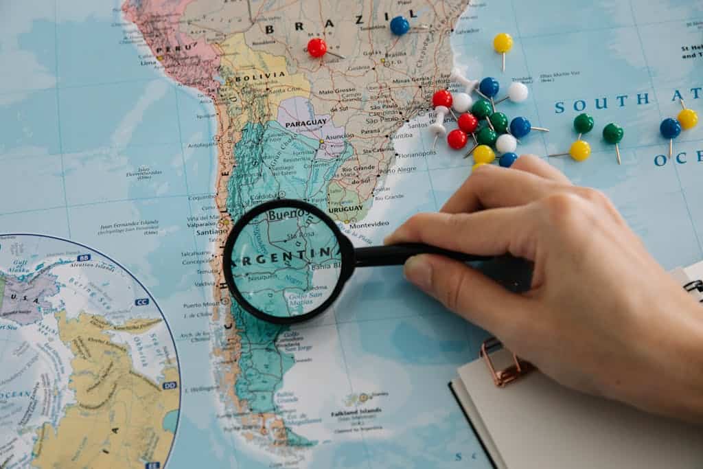Close-up of a hand examining a South America map with a magnifying glass, highlighting Patagonia in Argentina.